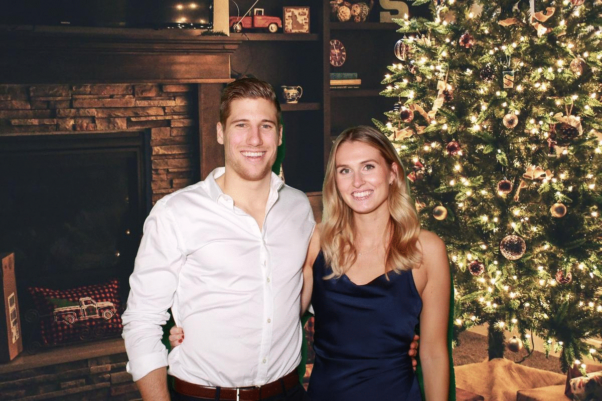 Man and woman stand in front of a green screen that changes into a christmans backdrop with a christmas tree on the right and fireplace on the left.